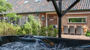 A hot tub in a backyard with a brick house, a wooden fence, and outdoor furniture. - Boerenzwaluw (Kamperveen)