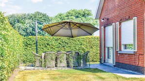 En rød murbygning med hvid garageport, en metalpergola og en hæk i baggrunden.