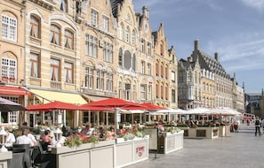 A row of outdoor cafes with red umbrellas, brick buildings, and outdoor seating.