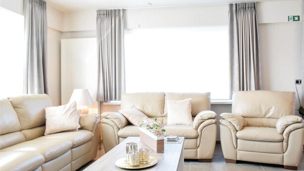 En moderne stue med beige lædersofaer, et træsofabord og et vindue med gardiner.