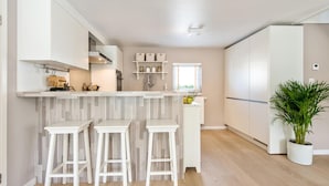 Une cuisine moderne avec des meubles blancs, un pare-feu en marbre et trois tabourets de bar blancs.