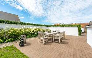 Une terrasse extérieure avec une table et des chaises, entourée d’un mur blanc recouvert de lierre.