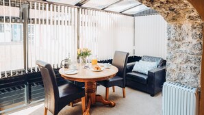 A cozy room with a round wooden table, two chairs, a black leather sofa, and a stone wall. - The Corn Store - UK6716 (Lydstep, near Tenby)
