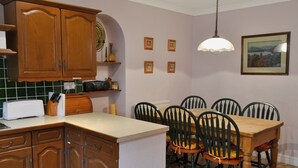 Uma cozinha com armários de madeira, uma mesa de jantar com cadeiras, uma torradeira e um lustre.