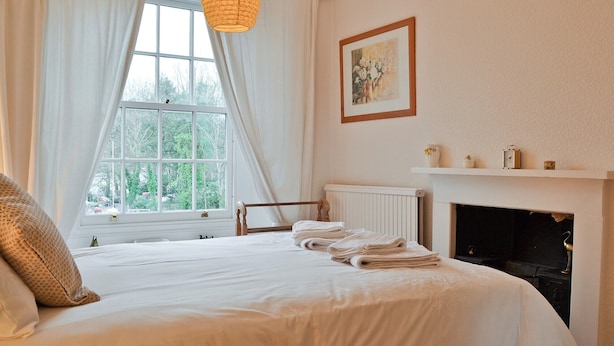 Quarto com cama grande, lareira, janela com cortinas e um quadro na parede.