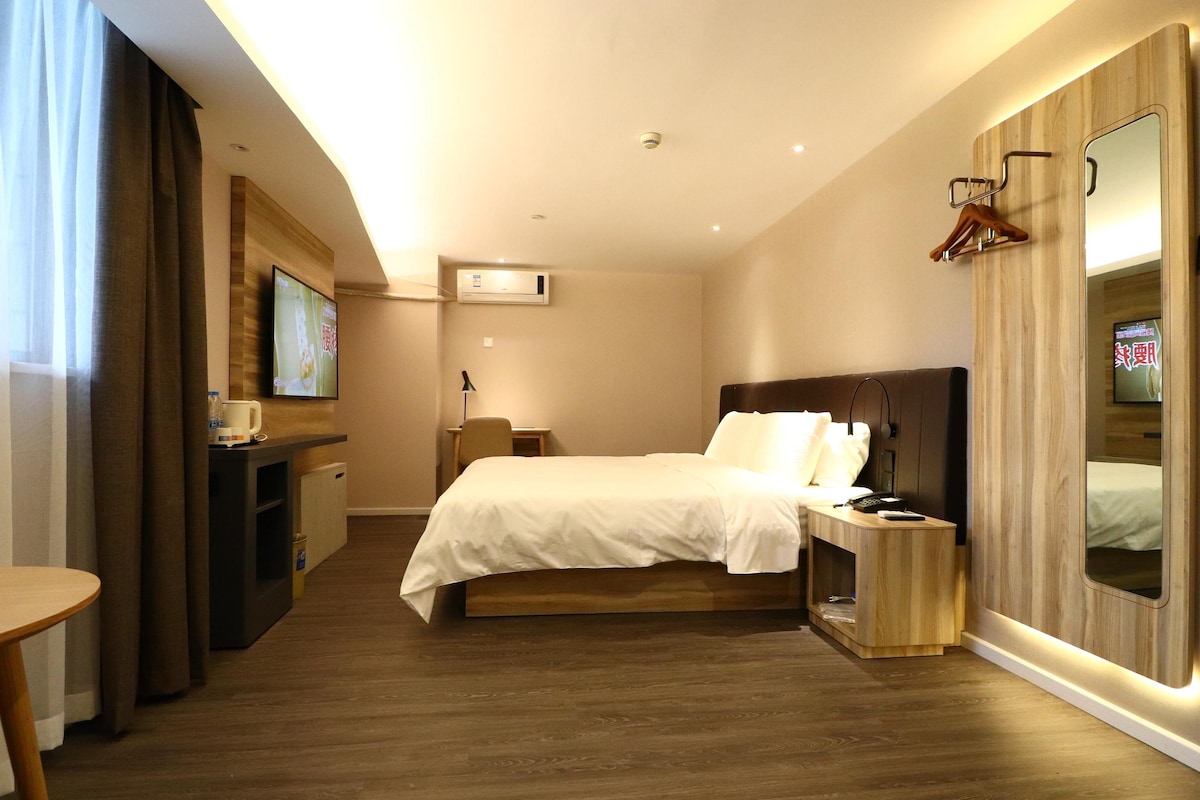 A hotel room with a bed, bedside table, TV, and a wardrobe.