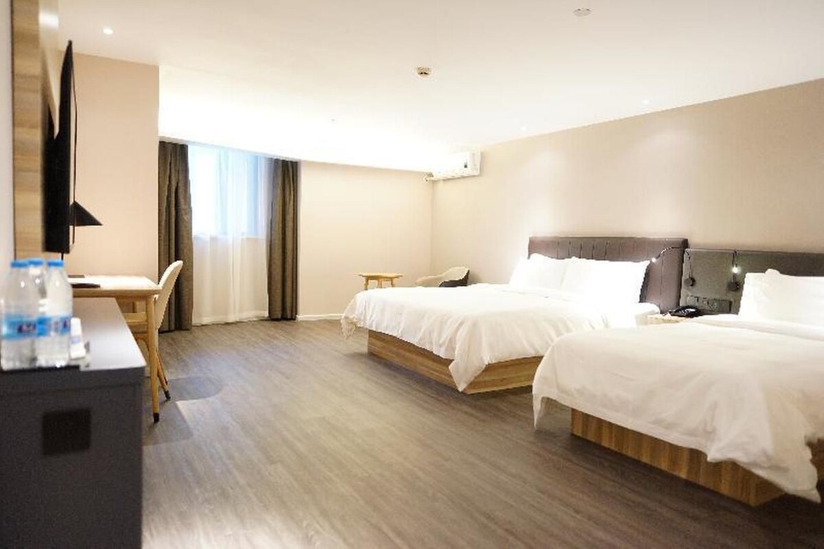A hotel room with two beds, a desk, a chair, and a television.