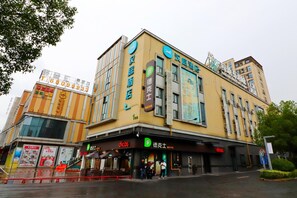 Un hotel con fachada amarilla, varios letreros incluido un logo 'D' destacado, y una entrada visible con gente afuera.