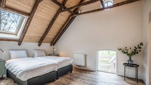 Una camera da letto con soffitto spiovente, un letto, un termosifone, una finestra e un piccolo tavolo con un vaso di fiori.