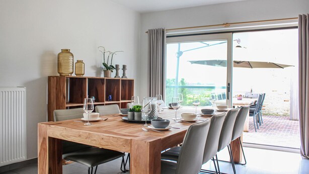 A dining area with a wooden table, chairs, and a view of the outdoors through large windows. - Amazing Home in Diksmuide With 5 Bedrooms and Wifi (Diksmuide)