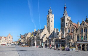 A historic town square with traditional European architecture, including a prominent clock tower and a variety of buildings with distinct facades.