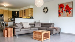 A modern living room with a grey sectional sofa, a wooden coffee table, and a dining area in the background. - Amazing Home in Diksmuide With 5 Bedrooms and Wifi (Diksmuide)