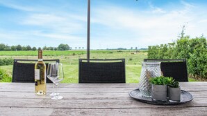 A wooden table with a wine bottle and glasses, two wicker chairs, and a tray with a glass jar and plants. - Amazing Home in Diksmuide With 5 Bedrooms and Wifi (Diksmuide)