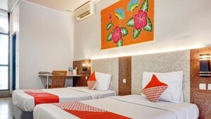 Ein Hotelzimmer mit zwei Betten, jeweils mit weißer Bettwäsche und roten Akzenten, einem Schreibtisch mit Stuhl und einem großen Blumenbild an der Wand.