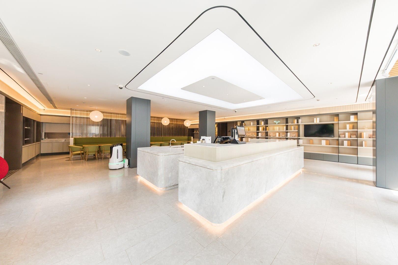 A modern hotel lobby with a central island, seating area, and a large TV screen.