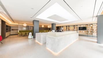 A modern hotel lobby with a central island, seating area, and a large TV screen.