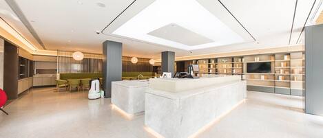 Un hall d’hôtel moderne doté d’un îlot central, d’un espace salon et d’un grand écran de télévision.
