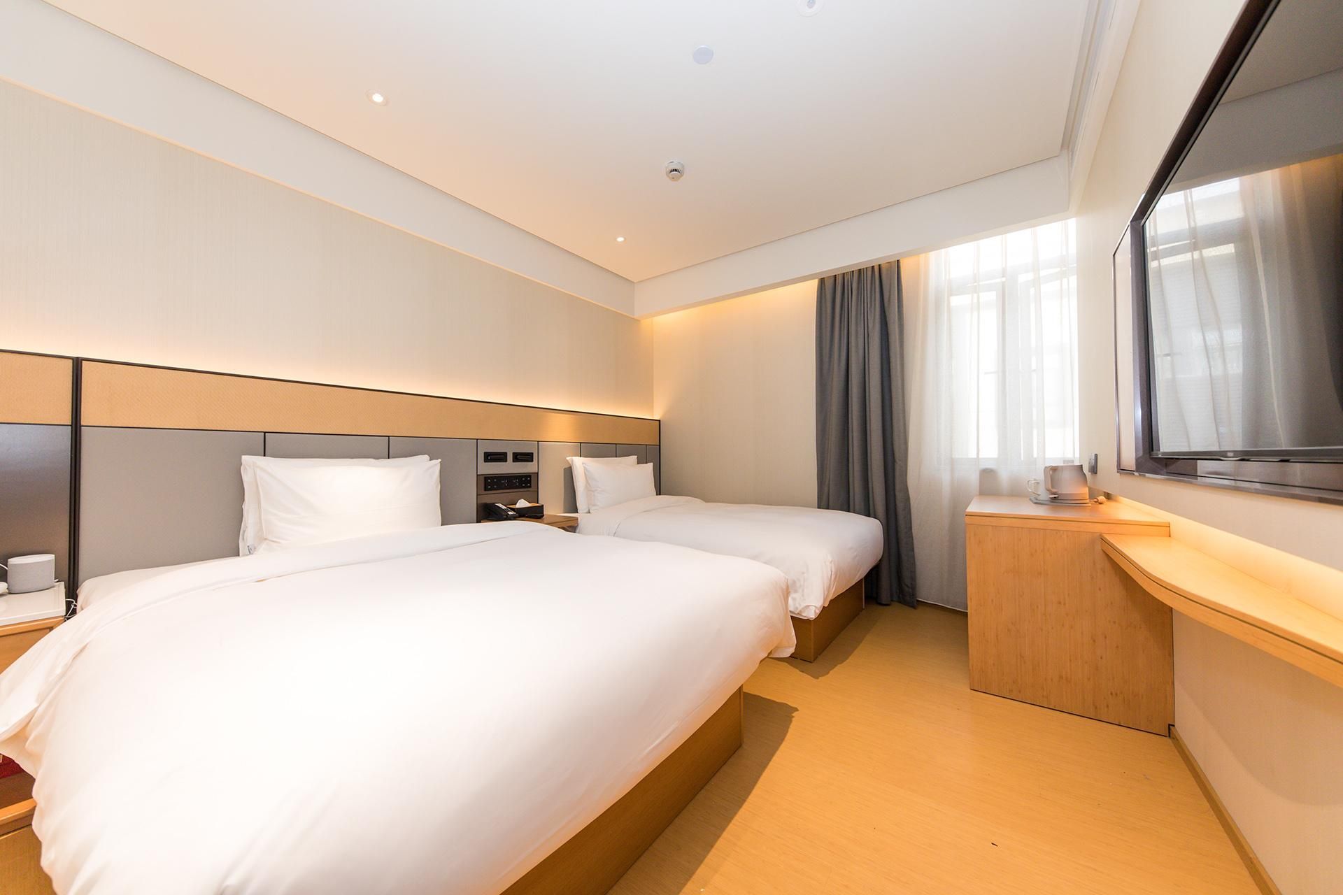 A hotel room with two beds, a desk, a mirror, and a window with curtains.