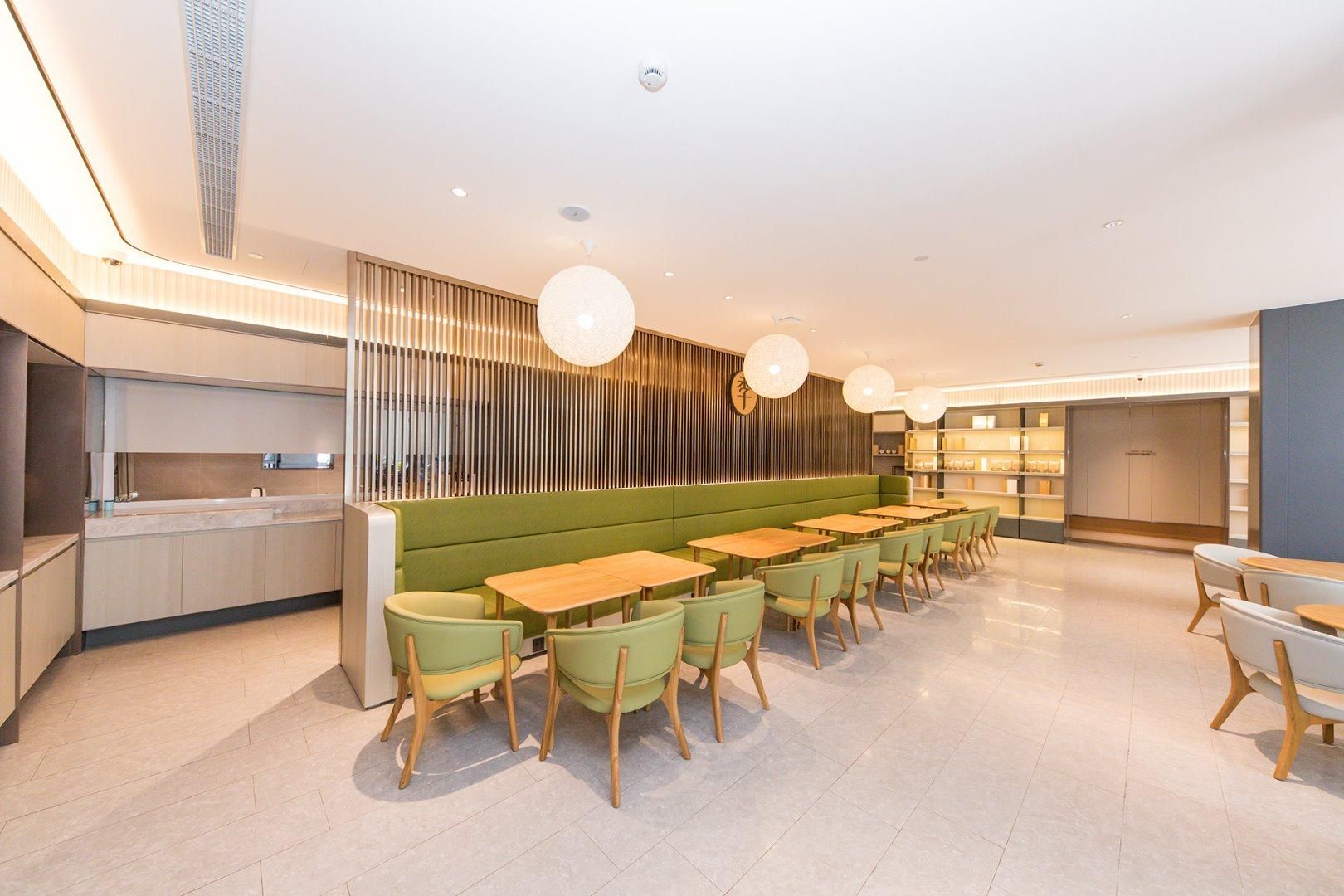 Un interior moderno con una zona de estar verde, mesas de madera e iluminación colgante.