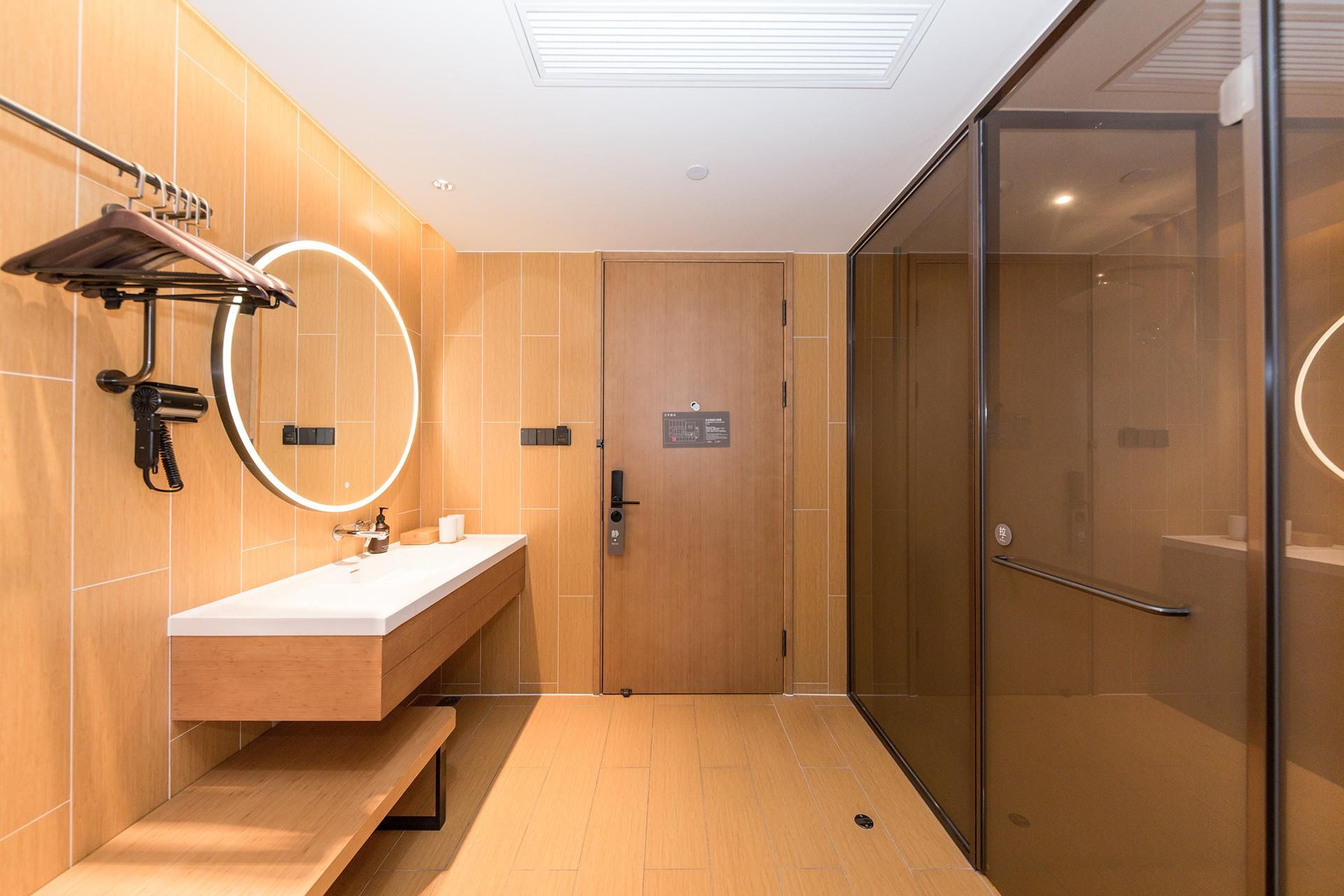A modern bathroom with a wooden vanity, a mirror with a light, a hairdryer, and a glass shower enclosure.