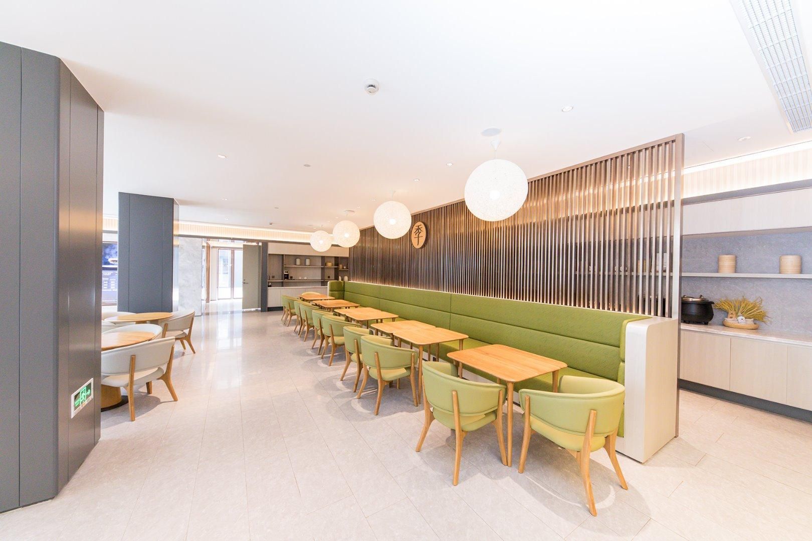 Un restaurante moderno con una barra larga, asientos verdes e iluminación colgante.