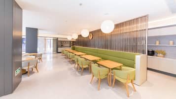A modern restaurant with a long counter, green seating, and pendant lighting.
