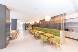 Moderni ravintola, jossa on pitkä baaritiskialue, vihreät istuimet ja riippuvalaisimet.