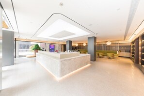 A modern hotel lobby with a central reception desk, seating area, and a large window. - Ji Hotel Shanghai Longbai Xincun Metro Station (Shanghai)