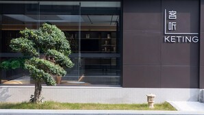 Ein modernes Gebäude mit Glasfassade, einem Schild mit der Aufschrift 'KETING' und einem kleinen Baum davor.
