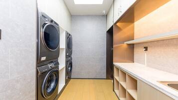 A compact laundry room with two front-loading washing machines, a countertop with a sink, and a skylight above.