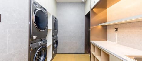 A compact laundry room with two front-loading washing machines, a countertop with a sink, and a skylight above.