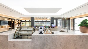 Eine moderne Hotelhalle mit einer zentralen Rezeption, einer großen Pflanze im Topf und Blick ins Freie.