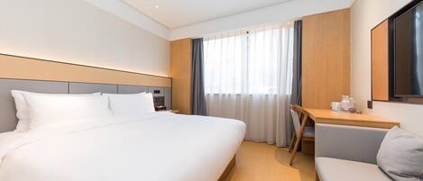 A hotel room with a bed, a desk, a chair, a sofa, and a large window with curtains.
