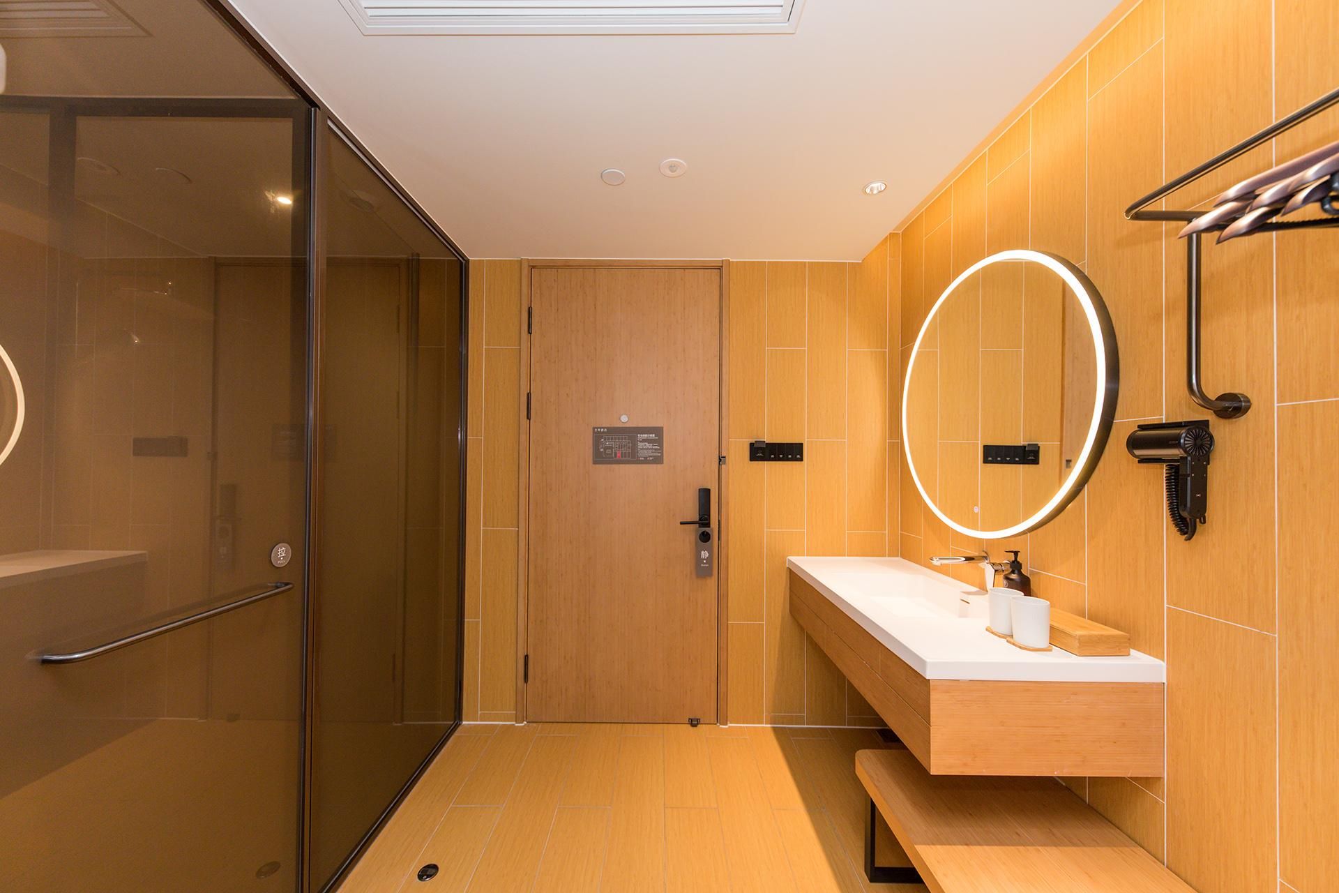 Un baño moderno con cabina de ducha de vidrio, un tocador de madera con espejo y un banco.