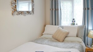 Een opgemaakt bed met opgevouwen handdoeken, een nachtkastje met een lamp en een decoratieve spiegel aan de muur.