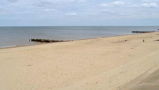 Een breed zandstrand met een houten pier die het water in loopt.