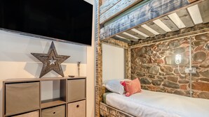 Una cama litera junto a una pared de piedra, con una decoración de estrella y una mesita de noche con cajas de almacenamiento.