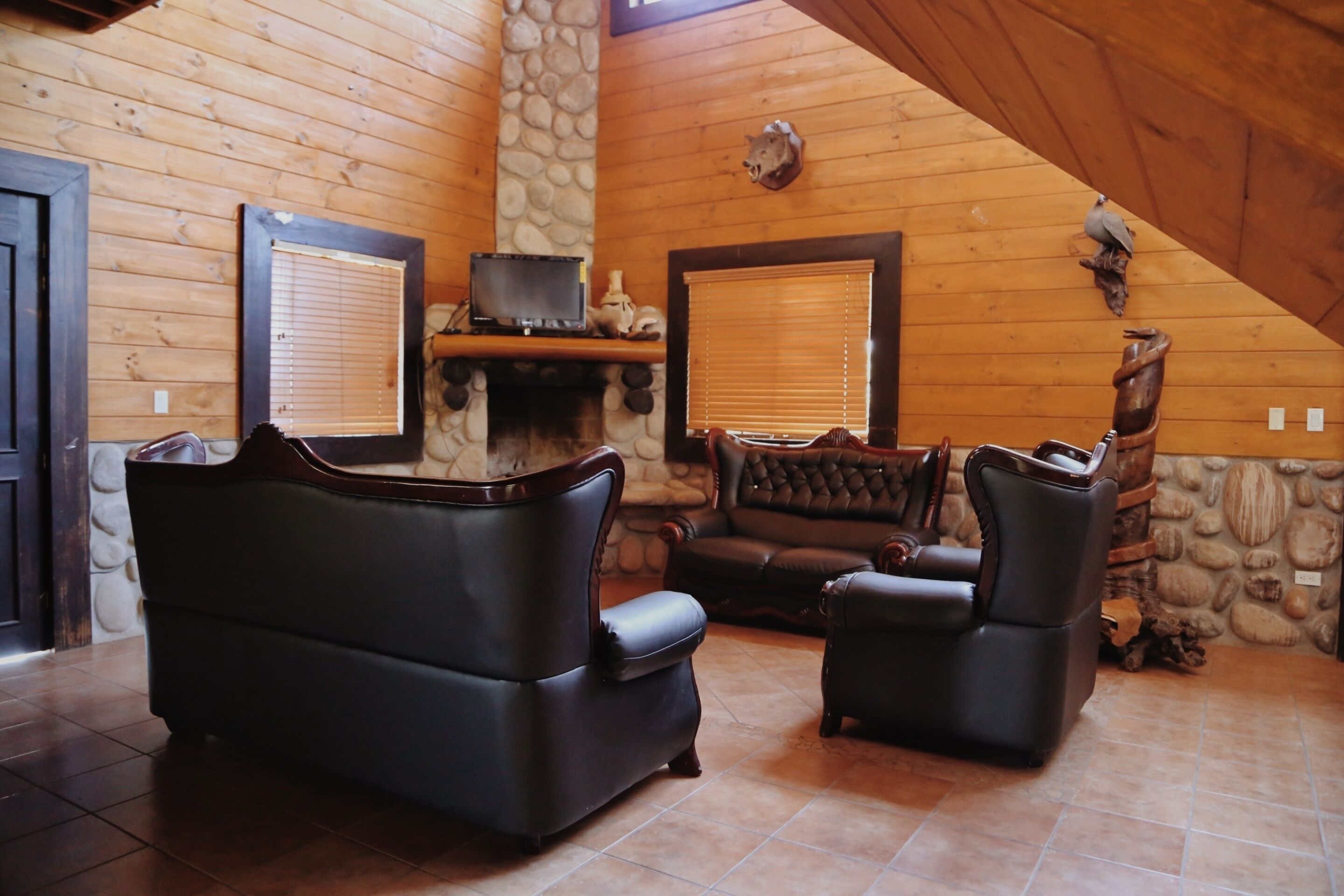 A cozy living room with a stone fireplace, leather sofas, and a stone wall.