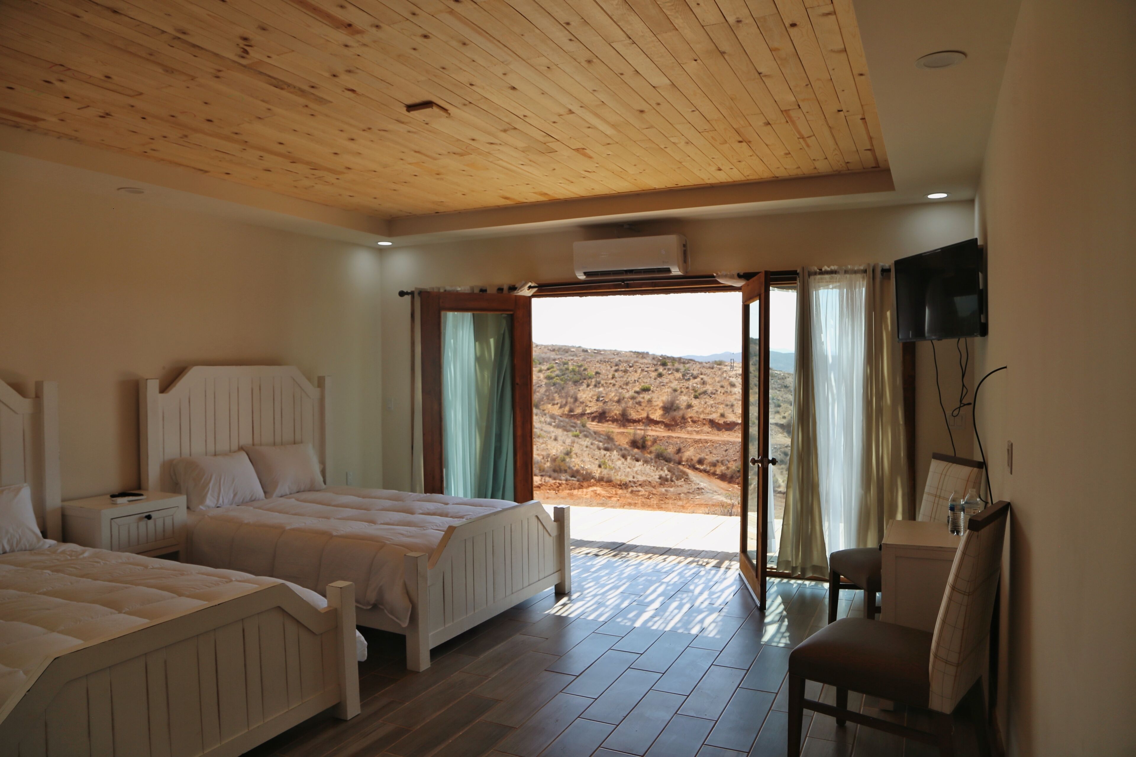 A bedroom with two beds, a TV, and a view of a desert landscape.