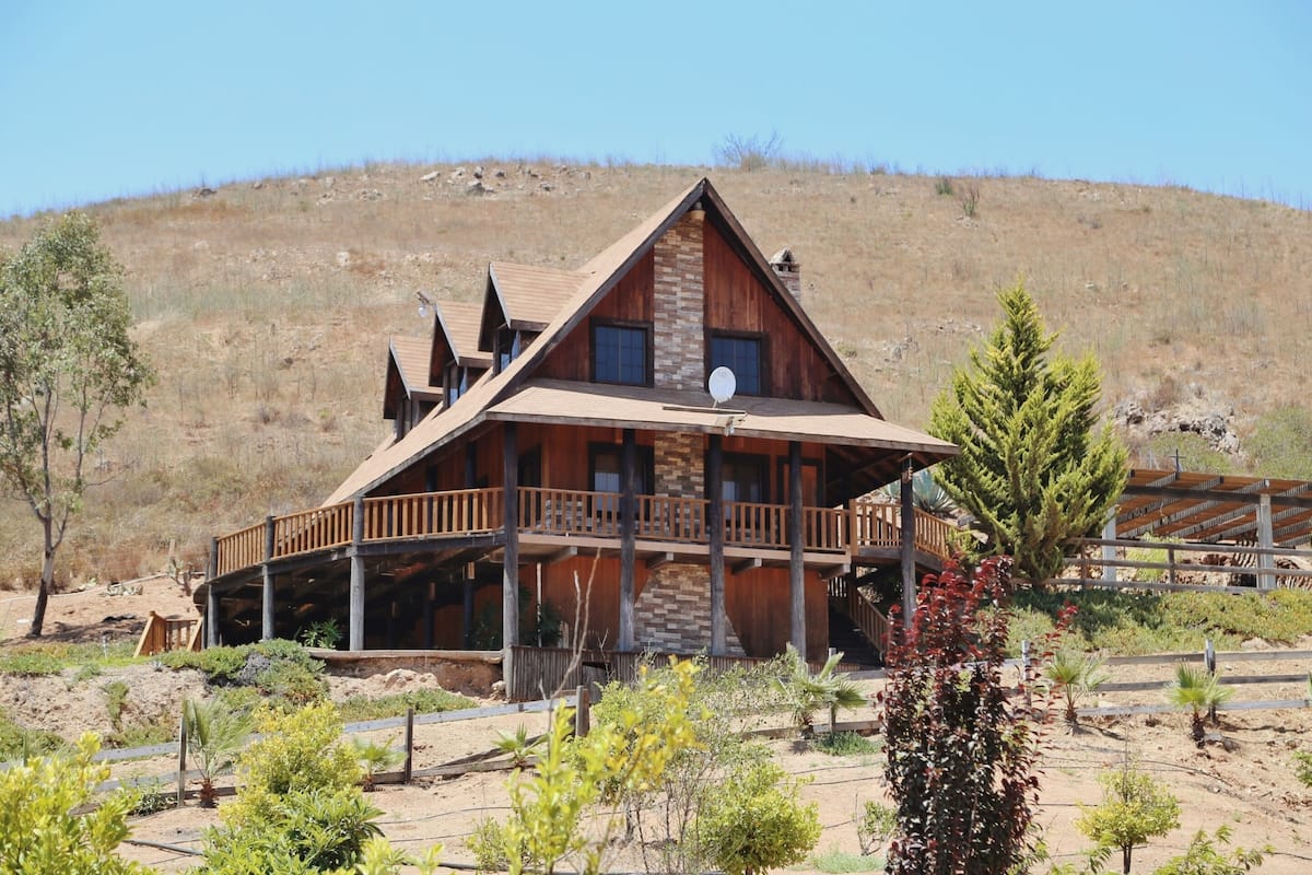 A wooden cabin with a balcony, surrounded by desert vegetation.