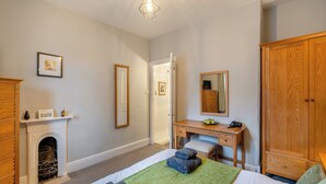 A bedroom with a bed, a desk, a wardrobe, a fireplace, and a mirror.