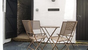 A patio with two folding chairs and a small round table, a black door, and a wall-mounted light fixture.
