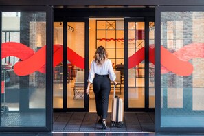 A person with a suitcase entering a building through a glass door with a red abstract design. - Hotel Moov Porto Alegre (Porto Alegre)