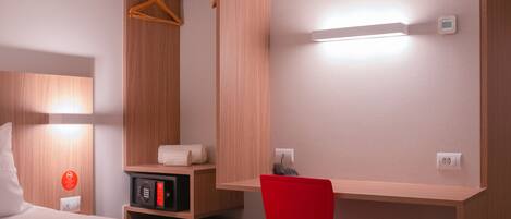 Habitación de hotel con cama, una silla roja, un armario de madera, un microondas y una mesita de noche con teléfono.