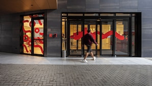 A building entrance with a glass door, a metal trash bin, and a paved walkway.