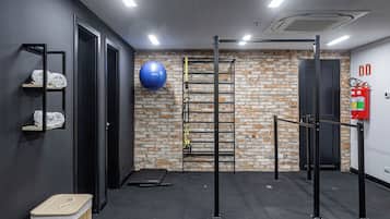 Un gimnasio con pared de ladrillo, barra de dominadas, pelota de ejercicio azul y extintor.