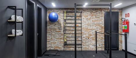 Un gimnasio con pared de ladrillo, barra de dominadas, pelota de ejercicio azul y extintor.