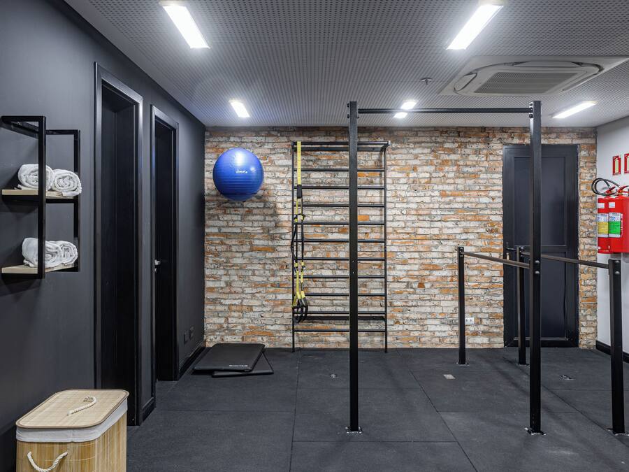 Academia com parede de tijolos, barra para puxar, bola de exercício azul e extintor de incêndio.