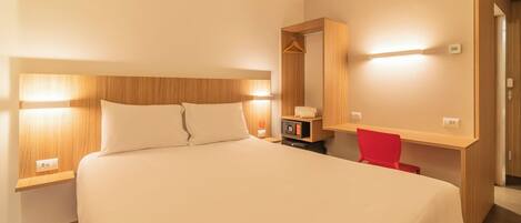 Quarto de hotel com uma cama grande, mesas de cabeceira, escrivaninha com cadeira, espelho e guarda-roupa.