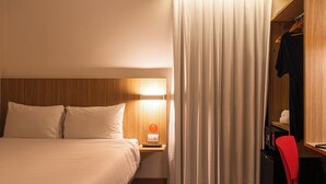 A hotel room with a bed, nightstand, lamp, curtains, and a red chair.